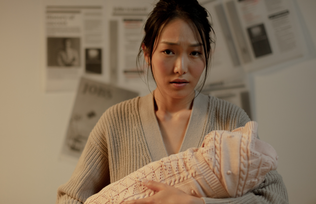 Postpartum mother standing and holding swaddled newborn with a distant expression, representing emotional disconnection as a sign of postpartum depression