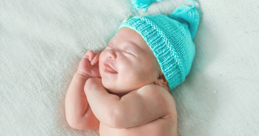 A smiling newborn baby wearing a blue hat showing early social and emotional development milestones.