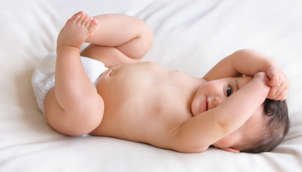 A happy infant lying on a white surface with legs raised and an alert, curious expression. This active, engaged state is ideal for introducing simple games like peekaboo that teach object permanence. Face-to-face play during awake windows supports cognitive development and strengthens the parent-baby connection in the first year of life.