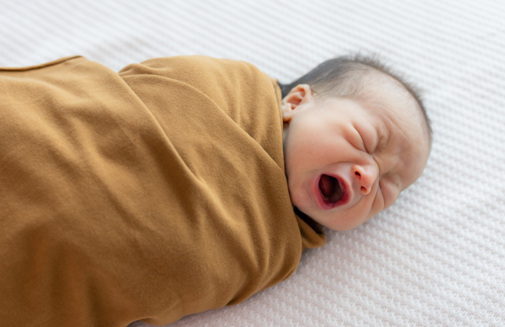 Swaddled newborn crying with eyes closed, representing common newborn eye concerns including blocked tear ducts and when to call the pediatrician