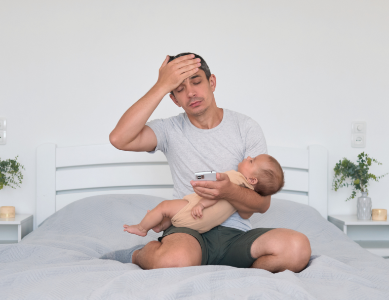 exhausted-dad-holding-newborn-on-bed-dad-burnout.jpg