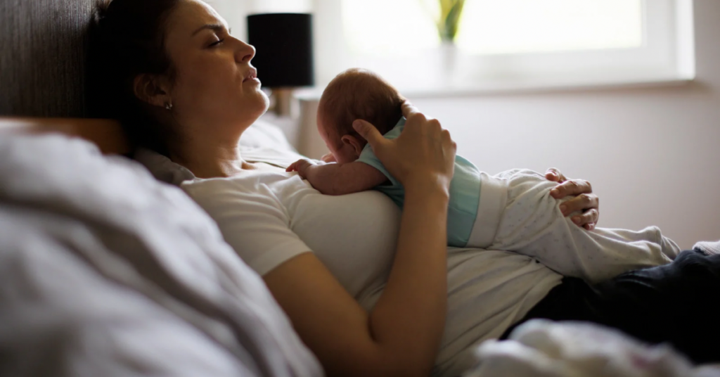  Exhausted postpartum mother resting in bed with her newborn lying on her chest during early days at home