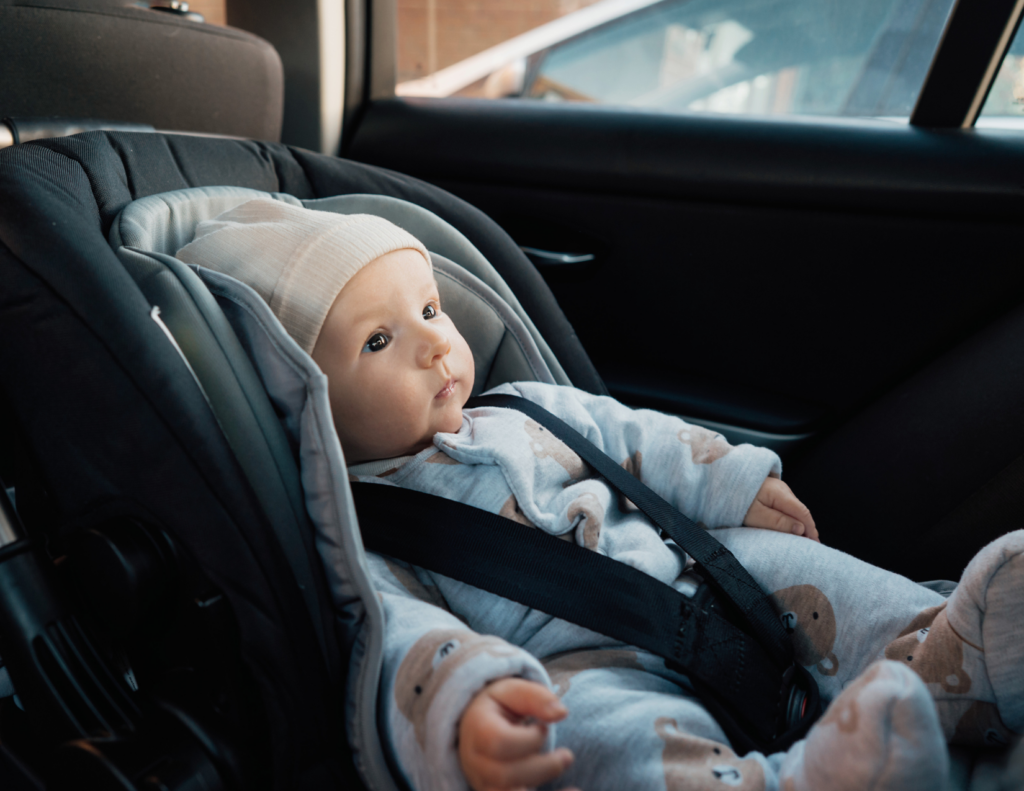 Alert newborn in a beige hat secured in a rear-facing infant car seat during the drive home from the hospital