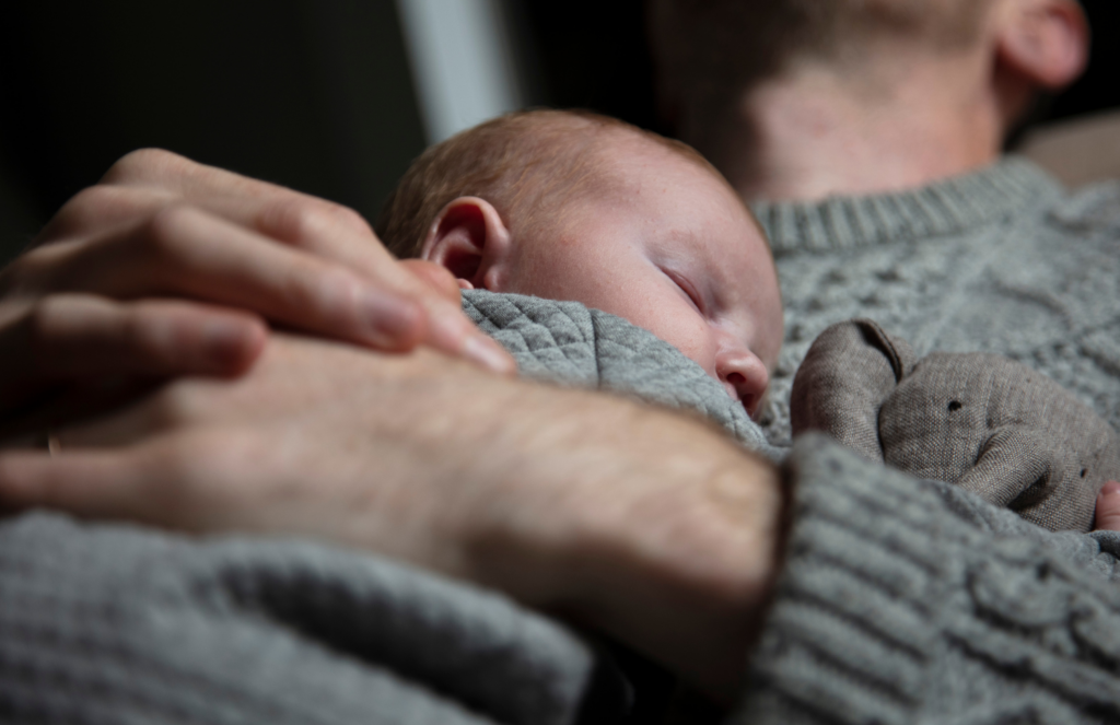 father holding sleeping newborn against chest during a calming bedtime routine, showing the comfort of skin-to-skin contact for infant sleep