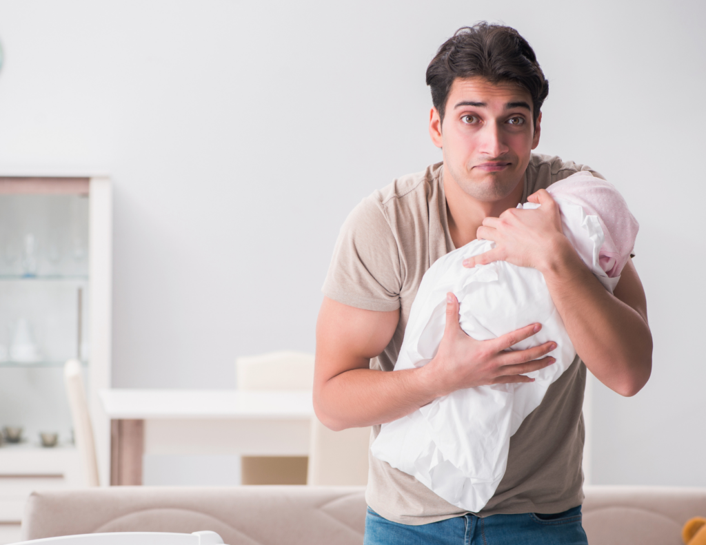 hat look every new dad knows — holding the baby, trying to figure it out, wondering why it feels harder than it looks.